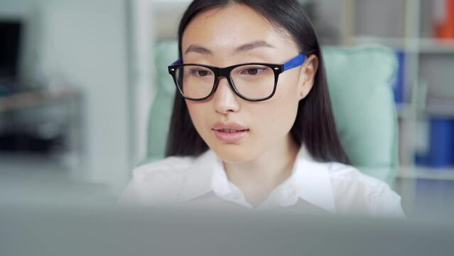 young asian business woman worker employee entrepreneur working on computer laptop sitting at desk at workplace in office. Close up Busy businesswoman in formal shirt and glasses using PC Asia Closeup