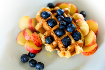 Homemade Belgian waffle decorated with blueberries and peach, breakfast concept