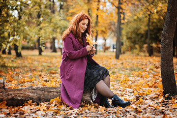 Mental health in autumn. Happy red-haired woman holding yellow maple autumn leaves