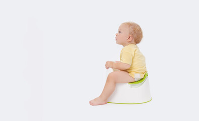 Potty training a baby. Little boy sitting on a potty next to a roll of toilet paper and diapers on...