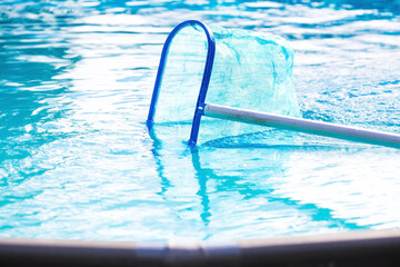 Cleaning a swimming pool with a metal frame with a net from leaves and dirt. Pool cleaner during...