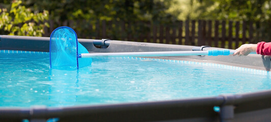 Cleaning a swimming pool with a metal frame with a net from leaves and dirt. Pool cleaner during...