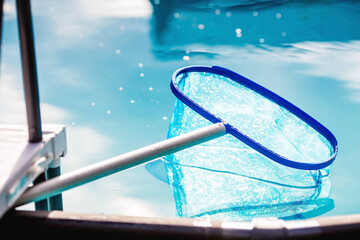 Cleaning a swimming pool with a metal frame with a net from leaves and dirt. Pool cleaner during work. Solar banner. The concept of summer holidays.