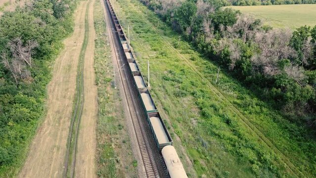 Long cargo bulk carrier train transporting wagons across rural landscape, aerial view
