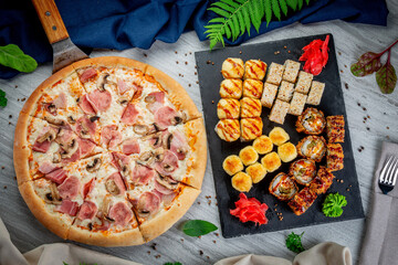Ham and mushroom pizza on shovel and roasted and baked set with sushi and rolls. Freshly baked with...