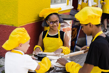 Multinational company of children cooks in yellow uniforms cooking dough for bakery. African...