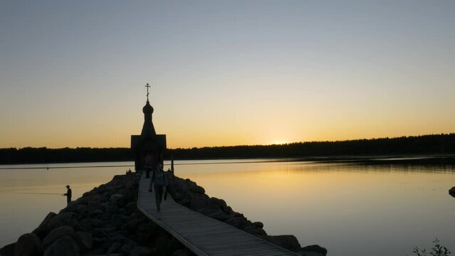 A man walks along the pier, against the backdrop of the chapel. The silhouette of a man against the background of the lake and the chapel.