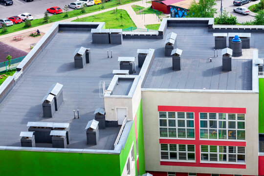 Top view dark flat roof with air conditioners and hydro insulation membranes modern school building residential area.