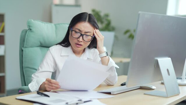 Difficult asian woman employee to deal with paperwork. documents. Stressed businesswoman confused by mistake, looking at camera through papers. bookkeeper, booker vaguely, dimly at work in office