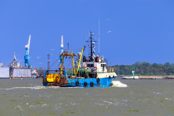 A small commercial fishing boat returns from the sea to the port. Seagulls accompany the boat