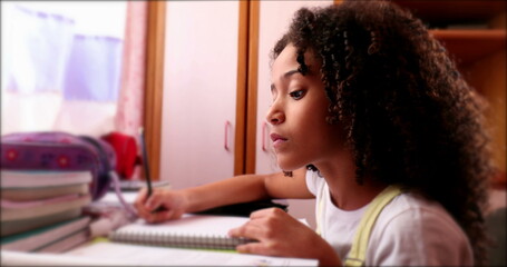 Little school girl studying at home writing notes. Black mixed race ethnicity child homework