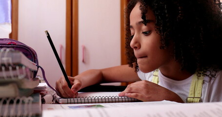 Little girl studying at home, mixed race child writing notes doing homework