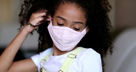 Little girl putting covid face mask, mixed race child puts mask