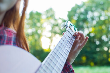 close up teenager girl plays guitar outside, country style