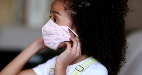 Little girl putting covid face mask, mixed race child puts mask