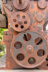 An old very large rusty piece of machinery with large metal gears, covers, and bolts.