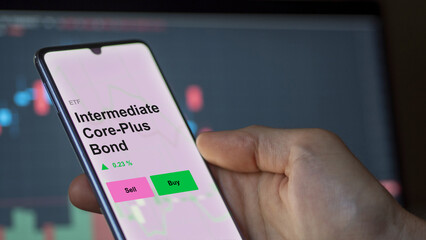 An investor's analizing the intermediate core-plus bond etf fund on a screen. A phone shows the prices of Intermediate core plus Bond