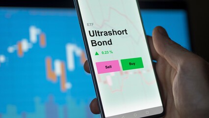 An investor's analizing the ultrashort bond etf fund on a screen. A phone shows the prices of ultra-short bond funds.