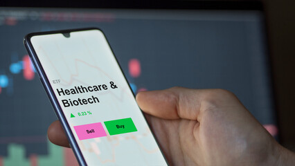 An investor's analizing the healthcare & biotech etf fund on a screen. A phone shows the prices of Healthcare & Biotech
