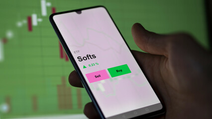 An investor's analizing the softs etf fund on a screen. A phone shows the prices of Softs