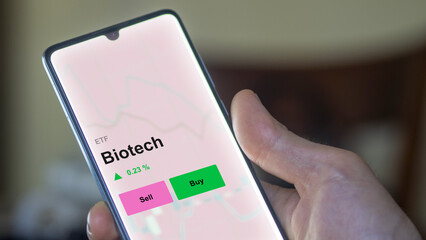 An investor's analizing the biotech etf fund on a screen. A phone shows the prices of Biotech