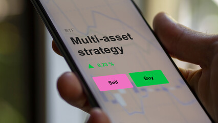 An investor's analizing the multi-asset strategy etf fund on a screen. A phone shows the prices of Multi-asset strategy
