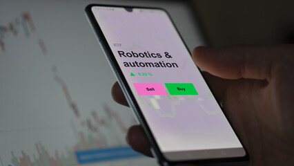 An investor's analizing the robotics & automation etf fund on a screen. A phone shows the prices of Robotics & automation