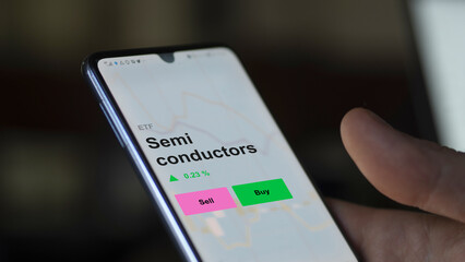 An investor's analizing the semi conductors etf fund on a screen. A phone shows the prices of Semi conductors