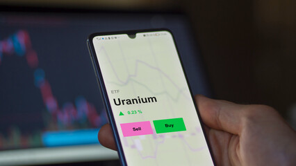 An investor's investing in an uranium etf fund on a screen to invest. A phone shows the prices of URANIUM - obrazy, fototapety, plakaty