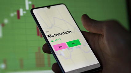 An investor's analizing the momentum etf fund on a screen. A phone shows the prices of Momentum