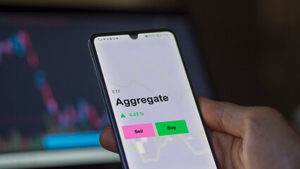 An investor's analizing the aggregate etf fund on a screen. A phone shows the prices of Aggregate
