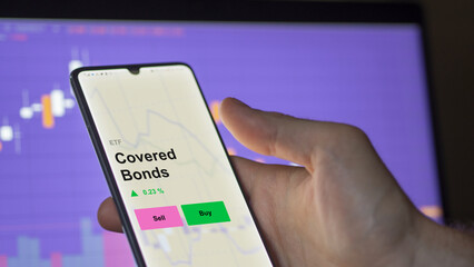 An investor's analizing the covered bonds etf fund on a screen. A phone shows the prices of Covered Bonds