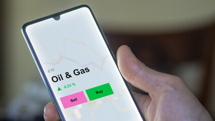 An investor's analizing the oil & gas etf fund on a screen. A phone shows the prices of Oil & Gas