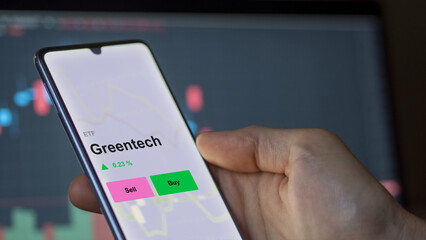An investor's analizing the greentech etf fund on a screen. A phone shows the price of green tech
