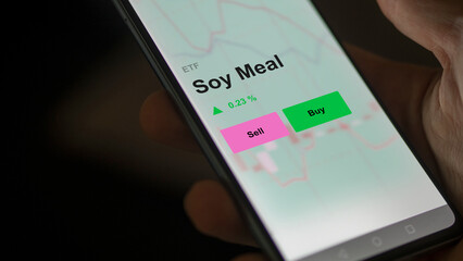 An investor's analizing the soy meal etf fund on a screen. A phone shows the prices of Soy Meal