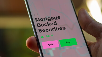 An investor's analizing the mortgage backed securities etf fund on a screen. A phone shows the prices of an ETF. 