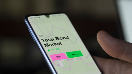 An investor's analizing the total bond market etf fund on a screen. A phone shows the prices of Total Bond Market