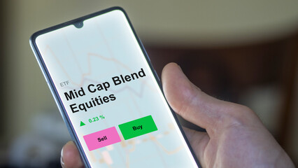 An investor's analizing the mid cap blend equities etf fund on a screen. A phone shows the prices of Mid Cap Blend Equities