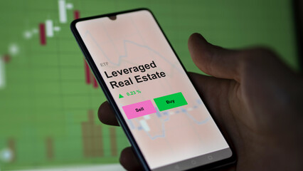 An investor's analizing the leveraged real estate etf fund on a screen. A phone shows the prices of Leveraged Real Estate