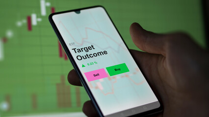 An investor's analizing the target outcome etf fund on a screen. A phone shows the prices of Target Outcome