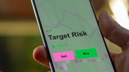 An investor's analizing the target risk etf fund on a screen. A phone shows the prices of Target Risk
