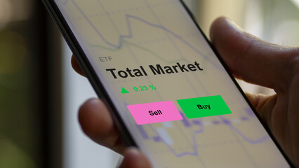 An investor's analizing the total market etf fund on a screen. A phone shows the prices of Total...