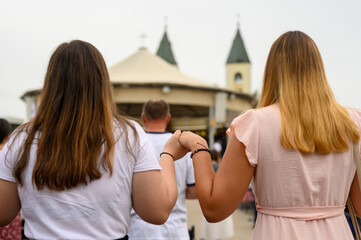 Two girls holding hands in prayer during Mladifest 2021 – the youth festival – in Medjugorje, Bosnia and Herzegovina. 2021-08-03. - obrazy, fototapety, plakaty