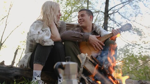Slow motion 2x Closeup portrait of a couple sitting with guitar near bonfire in the forest.