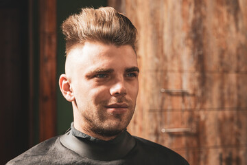 Portrait of a young unshaven man in a barbershop during a haircut