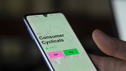 An investor's analizing the consumer cyclicals etf fund on a screen. A phone shows the prices of Consumer Cyclicals