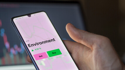 Un investisseur analyse le fonds ETF environnement sur un écran. Un téléphone affiche les prix des ETF verts, des fonds durables, texte en anglais.