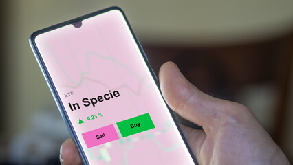 An investor's analizing the in specie etf fund on a screen. A phone shows the prices of In Specie