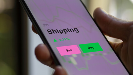 An investor's analizing the shipping etf fund on a screen. A phone shows the prices of Shipping