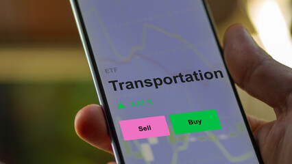 An investor's analizing the transportation etf fund on a screen. A phone shows the prices of Transportation